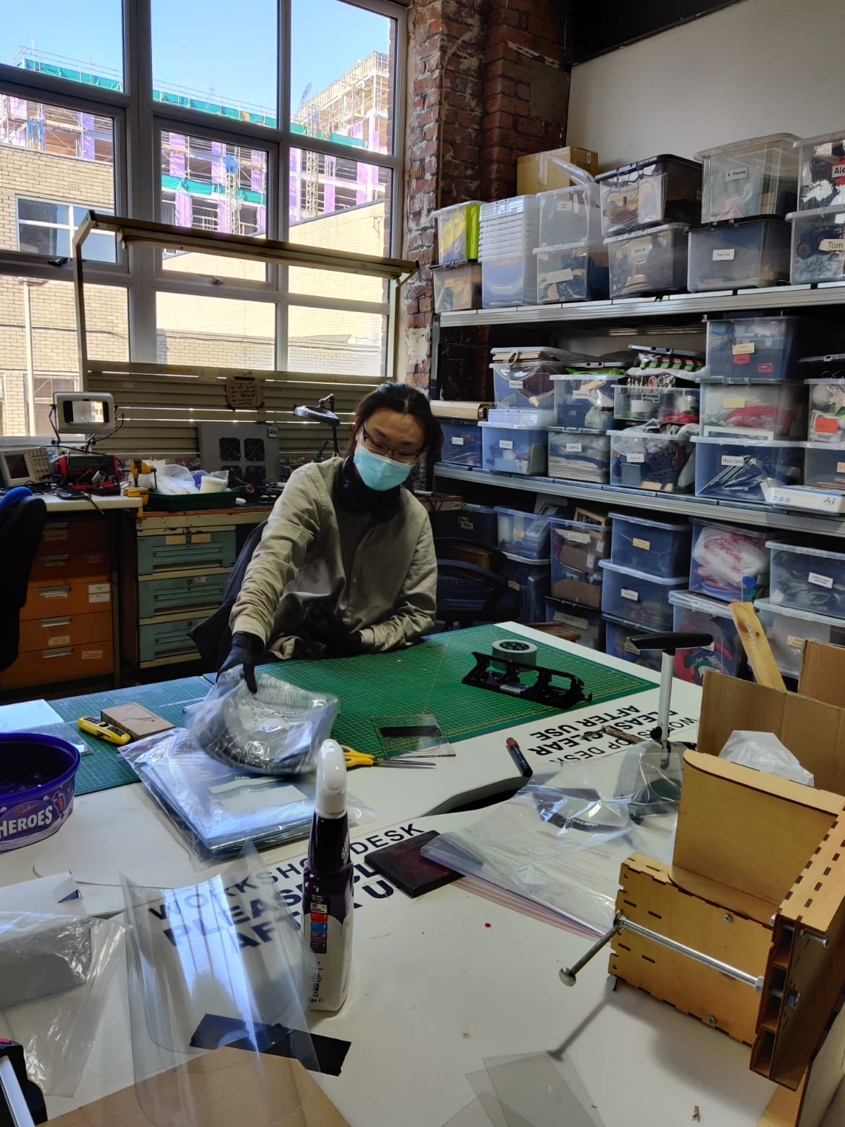 A person wearing a surgical mask sits at a desk in the DoES Liverpool workshop, making visors for our pandemic response